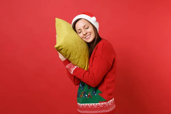 Relaxed young Santa girl in Christmas hat holding pillow keeping eyes closed sleeping isolated on bright red wall background. Happy New Year 2019 celebration holiday party concept. Mock up copy space