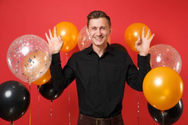 Genç gülümseyen klasik siyah tişörtlü adam meditasyon parlak kırmızı arka plan hava balonları Yayilim ellerinde. St. Valentine's Dünya Kadınlar Günü mutlu yeni yıl Doğum günü mockup tatil parti konsept