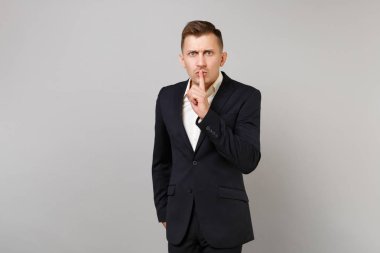 Sıkı genç iş adamı hush söyleyerek klasik siyah takım elbise gömlek gri arka plan üzerinde izole dudaklar shhh jest parmağında ile sessiz ol. Başarı kariyer servet iş kavramı. Kopyalama alanı alay