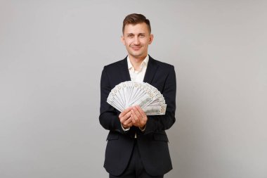 Klasik siyah elbiseli Genç iş adamı gülümseyen, gömlek holding çok dolar banknotlar, nakit para üzerinde gri arka plan izole sürü. Başarı kariyer servet iş kavramı. Kopyalama alanı alay