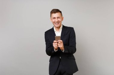 Genç gülüyor iş adamı klasik siyah takım elbise, gömlek cep telefonuyla Studio gri arka plan üzerinde izole sms mesajı yazarak. Başarı kariyer servet iş kavramı. Kopyalama alanı alay