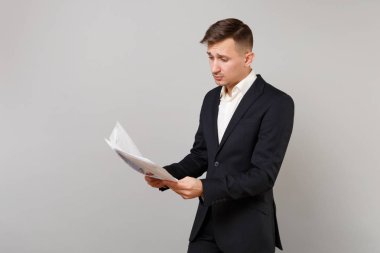 Dalgın genç iş adamı klasik siyah takım elbise, holding, gri duvar arka planda Studio izole kağıt belgeler üzerinde seyir gömlek. Başarı kariyer servet iş kavramı. Kopyalama alanı alay
