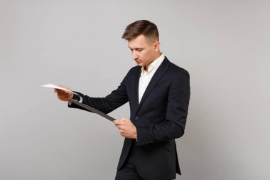 Undistracted genç iş adamı klasik siyah elbiseli holding, gri arka plan üzerinde izole kağıtları belgeyle panoya arıyorum. Başarı kariyer servet iş kavramı. Kopyalama alanı alay