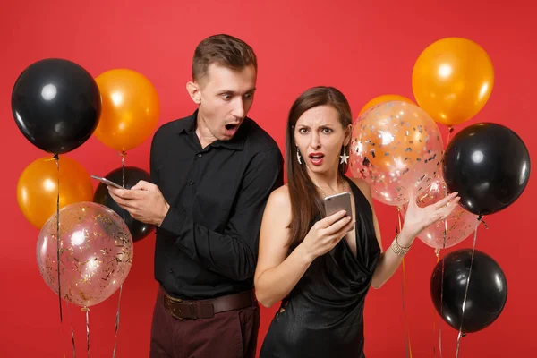 Couple stand back to back messaging in cellphone celebrating birthday holiday party isolated on red background air balloons. St. Valentine International Women Day Happy New Year 2019 concept. Mock up