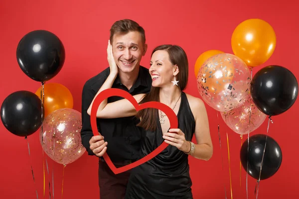 Loving couple in black clothes hold heart celebrating birthday holiday party isolated on bright red background air balloons. St. Valentine International Women Day Happy New Year 2019 concept. Mock up