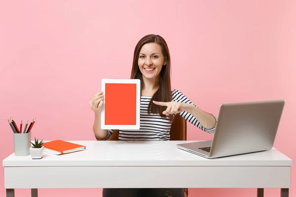 女性空画面とタブレット コンピューターで人差し指を笑顔で ピンクの背景に分離された現代 のラップトップでの白の机に座って仕事 ビジネス キャリアを達成 コピー スペース — ストック写真