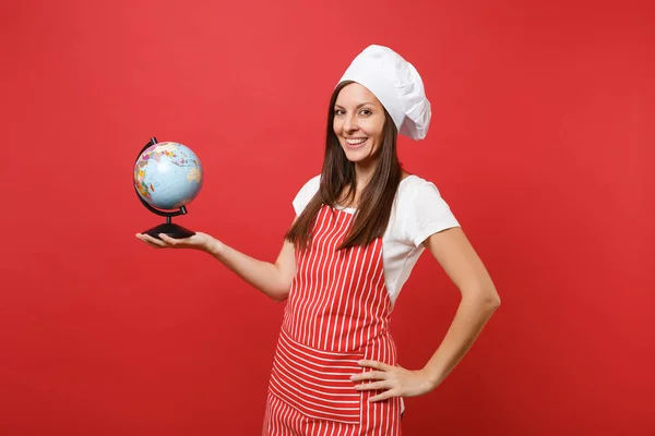 Housewife female chef cook or baker in striped apron, white t-shirt, toque chefs hat isolated on red wall background. Housekeeper woman holding in palms Earth world globe. Mock up copy space concept