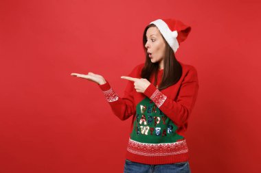 Sürpriz işaret eden bir ele, işaret parmağı bir kenara izole kırmızı zemin üzerine ağız geniş açık tutarak şok Noel Baba kız. Mutlu yeni yıl 2019 kutlama tatil parti kavramı. Kopyalama alanı alay
