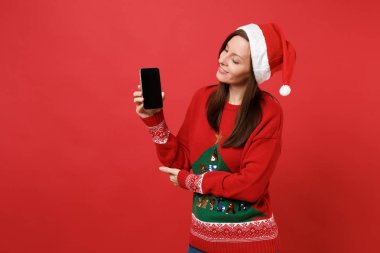 Boş boş ekran ile cep telefonuna el arıyorsunuz Noel şapkalı Noel Baba kız izole kırmızı zemin üzerine ihale genç. Mutlu yeni yıl 2019 kutlama tatil parti kavramı. Kopyalama alanı alay