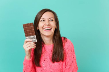 Örgü pembe kazaklı bir kenara tutun el çikolata bar bakarak gülen güzel genç kız mavi turkuaz duvar arka plan stüdyo portre üzerinde izole. İnsanlar yaşam tarzı kavramı. Kopyalama alanı alay