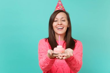 Örgü pembe kazak ve Doğum günü şapkası elinde mavi turkuaz duvar arka plan stüdyo portre üzerinde izole mum ile pasta holding neşeli genç kadın. İnsanlar yaşam tarzı kavramı. Kopyalama alanı alay