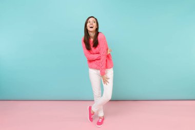 Tam uzunlukta örme gül kazaklı gülümseyen genç kadın portresi, beyaz parlak pembe mavi pastel duvar arka planda Studio izole poz pantolon. Moda yaşam tarzı kavramı. Kopyalama alanı alay