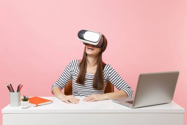 Genç gülümseyen kadın rahat kıyafetler içinde kulaklık başında sanal gerçekliğin oturmak ve pastel pembe izole pc laptop beyaz masa başında çalışmak. Başarı iş kariyer kavramı. Kopya alanı