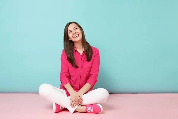 纵向微笑的年轻女子在玫瑰衬衫衬衫 白色裤子坐在地板上查出明亮的粉红色蓝色蜡笔墙背景工作室时尚生活方式概念 模拟复制空间 — 图库照片