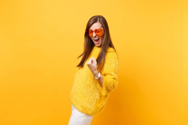 Kürk kazaklı, çok memnun genç kadın kalp turuncu gözlük Evet diyerek kazanan jest yapıyor parlak sarı arka plan üzerinde izole çığlık. İnsanlar samimi duygular, yaşam kavramı. Reklam alanı