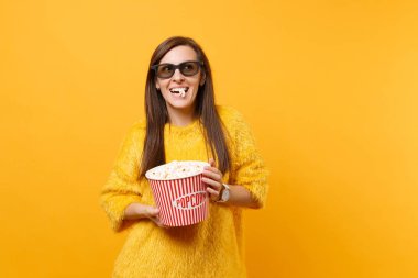 Neşeli mutlu genç kız film film izlerken ve parlak sarı arka plan üzerinde izole kova patlamış mısır yemek 3d IMAX bardaklarda portresi. Sinema, yaşam kavramı insanların samimi duygular