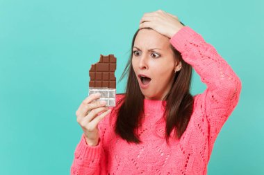 Örgü pembe kazak holding izole mavi duvar arka plan stüdyo portre üzerinde kafa el koyarak elinde çikolata şok endişe genç kadın. İnsanlar yaşam tarzı kavramı. Kopyalama alanı alay