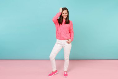 Tam uzunlukta örme gül kazaklı gülümseyen genç kadın portresi, beyaz parlak pembe mavi pastel duvar arka planda Studio izole poz pantolon. Moda yaşam tarzı kavramı. Kopyalama alanı alay