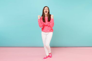 Tam uzunlukta örme gül kazaklı gülümseyen genç kadın portresi, beyaz parlak pembe mavi pastel duvar arka planda Studio izole poz pantolon. Moda yaşam tarzı kavramı. Kopyalama alanı alay