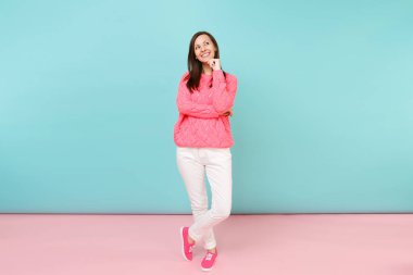 Tam uzunlukta örme gül kazaklı gülümseyen genç kadın portresi, beyaz parlak pembe mavi pastel duvar arka planda Studio izole poz pantolon. Moda yaşam tarzı kavramı. Kopyalama alanı alay