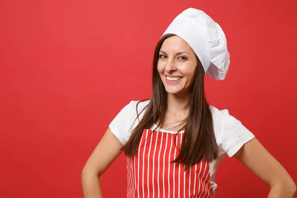 Housewife female chef cook or baker in red striped apron, white t-shirt, toque chefs hat isolated on red wall background. Close up portrait of housekeeper brunette woman. Mock up copy space concept