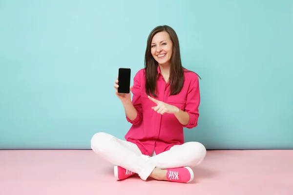 在玫瑰衬衫白色裤子坐在地板上保持手机隔离在明亮的粉红色蓝色柔和的墙壁背景工作室的年轻有趣的妇女全长纵向 时尚生活理念 模拟复制空间 — 图库照片