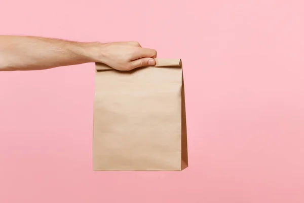 Erkek el kahverengi temizleme boş boş craft kağıt ihale için paket servisi olan restoran pastel pembe arka plan üzerinde izole kapatmak. Ambalaj şablon kadar sahte. Teslim hizmet anlayışı kopyalama alanı reklam alanı