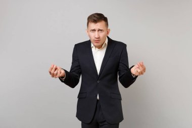 Çapraşık genç iş adamı klasik siyah takım elbise sürtünme parmaklar, nakit hareketi, gri arka plan üzerinde izole para talebinde gösterilen. Başarı kariyer servet iş kavramı. Kopyalama alanı alay