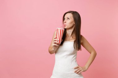 Ayakta, plastik kap pastel pembe izole bir yana ve içme kola veya kola bakmak beyaz gelinlik güzel gelin kadın portresi. Düğün kutlama kavramı. Kopya alanı