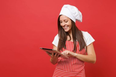 Ev hanımı kadın şef aşçı ya da baker izole kırmızı duvar arka plan üzerinde çizgili önlük, beyaz tişört, toque şefler şapkalı. Eğlenceli kahya kadın tablet pc tarifi arıyorum. Kopyalama alanı kavramı alay