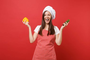 Ev hanımı kadın şef aşçı ya da baker Studio kırmızı duvar arka plan üzerinde izole çizgili önlük, beyaz tişört, toque şefler şapkalı. Kadın sarı biber, yeşil salatalık tutun. Kopyalama alanı kavramı alay