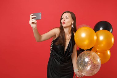 Güzel kadın siyah dudak şişirme elbise, hava balonları alarak selfie cep telefonu kırmızı zemin üzerine izole atış yapıyor tutarak hava öpücük göndermek. Mutlu yeni yıl Doğum günü mockup tatil parti konsept