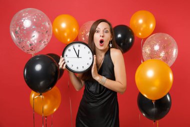 Şok genç kadın siyah elbiseli kırmızı arka plan hava balonu üzerinde yuvarlak saat tutan kutluyor. Zaman tükeniyor. Dünya Kadınlar günü, mutlu yeni yıl, Doğum günü mockup tatil parti konsept