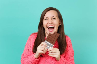 Neşeli genç kız elinde tutan ve mavi turkuaz duvar arka planda, stüdyo portre izole çikolata yeme örme pembe kazaklı gülüyor. İnsanlar yaşam tarzı kavramı. Kopyalama alanı alay