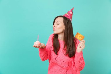 Örgü pembe kazaklı, Doğum günü şapka kapalı gözler kek, üzerine de mum dışarı üfleme ile ihale genç kız kredi kartı üzerinde mavi arka plan izole elinde tut. İnsanlar yaşam tarzı kavramı. Kopyalama alanı alay