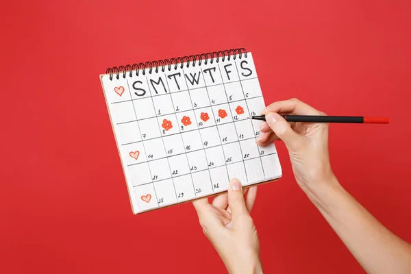 Close up female holds in hand red pencil female periods calendar for checking menstruation days isolated on trending red wall background. Medical healthcare gynecological concept. Copy space. Mock up