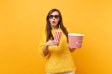 Concerned woman in 3d imax glasses pointing index finger, watching movie film holding bucket of popcorn cup of cola or soda isolated on yellow background. People sincere emotions in cinema, lifestyle clipart