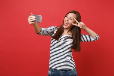 Cep telefonu parlak kırmızı zemin üzerine izole zafer işaret gösteren çizgili kıyafetler alarak selfie yapıyor neşeli genç kadını vurdu. İnsanlar samimi duygular, yaşam kavramı. Kopyalama alanı alay