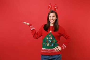 Güzel genç Noel Baba kız örme kazaklı, dekoratif geyik boynuzları işaret eden bir ele bir kenara izole kırmızı zemin üzerine kafa eğlenceli. Mutlu yeni yıl 2019 kutlama tatil parti kavramı. Kopyalama alanı alay