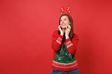 Kazaklı genç Noel Baba kız gülümseyerek, yukarıya bakıyor, yüzünde kırmızı zemin üzerine izole ellerini koyarak dekoratif geyik boynuzları eğlenceli. Mutlu yeni yıl 2019 kutlama tatil parti kavramı. Kopyalama alanı alay