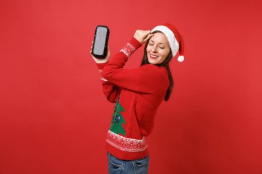 Genç ve güzel Noel Baba kız gözlerini tutmak taşınabilir kablosuz bluetooth müzik hoparlör izole kırmızı zemin üzerine tutarak kapalı. Mutlu yeni yıl 2019 kutlama tatil parti kavramı. Kopyalama alanı alay