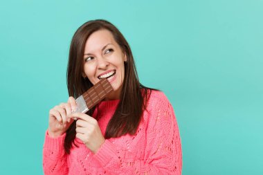 Genç ve güzel kadın elinde bir kenara izole mavi turkuaz duvar arka planda, stüdyo portre seyir bar çikolata ısırmak pembe kazak holding ördü. İnsanlar yaşam tarzı kavramı. Kopyalama alanı alay