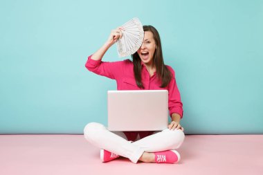 Tam uzunlukta gül gömlek bluz genç kadın portresi, beyaz pantolon katta oturan pembe mavi pastel duvar arka plan studio izole para pc tutun. Moda yaşam tarzı kavramı. Kopyalama alanı alay