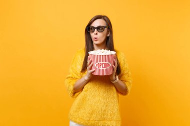 Şüpheli şaşkın genç kız bir kenara tutan kova patlamış mısır film film arıyorum izlerken 3d IMAX bardaklarda parlak sarı arka plan üzerinde izole. Sinema, yaşam kavramı insanların samimi duygular