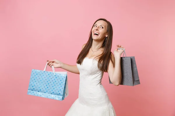 愉快的新娘妇女的肖像在婚纱礼服看拿着五颜六色的包裹袋与购买后 购物孤立在粉红色的背景 婚礼概念的组织 复制空间 — 图库照片