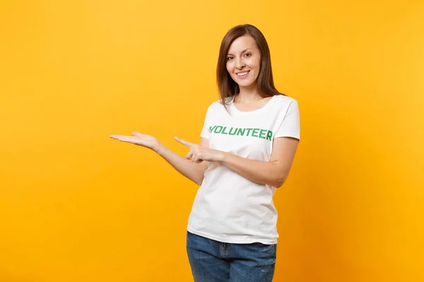 Portrait of happy smiling satisfied woman in white t-shirt with written inscription green title volunteer isolated on yellow background. Voluntary free assistance help, charity grace work concept