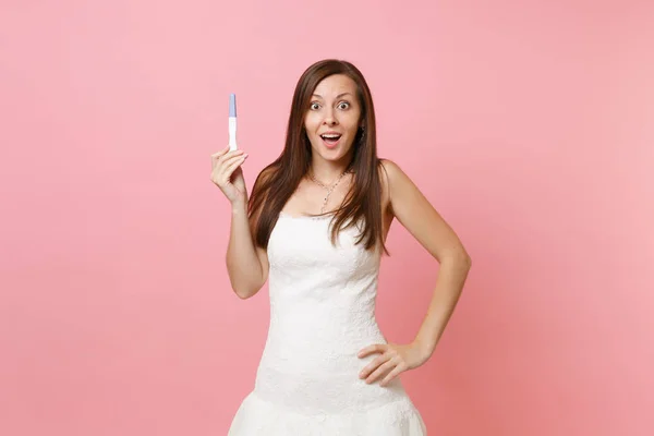 パステル ピンクの背景に分離された妊娠テストを保持している白いウェディング ドレスでショックを受けた花嫁女性を興奮させた 医療医療婦人科妊娠不妊治療出産の人概念 コピー スペース — ストック写真