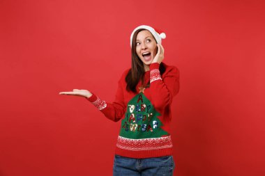 Bir kenara izole kırmızı zemin üzerine el işaret neşeli genç Santa şapkalı kız yakınındaki yüz, el ayak uydurarak arıyorsunuz Noel. Mutlu yeni yıl 2019 kutlama tatil parti kavramı. Kopyalama alanı alay