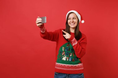 İşaret parmağı parlak kırmızı zemin üzerine izole alarak selfie üstünde hareket eden telefon, atış yapıyor gülümseyen genç Noel Baba kız. Mutlu yeni yıl 2019 kutlama tatil parti kavramı. Kopyalama alanı alay
