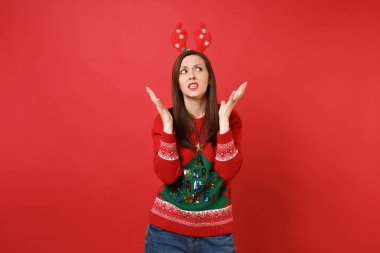 Örme kazak, şaşkın genç Noel Baba kız eğlenceli dekoratif geyik boynuzları eller izole kırmızı zemin üzerine yayılan arıyorum. Mutlu yeni yıl 2019 kutlama tatil parti kavramı. Kopyalama alanı alay